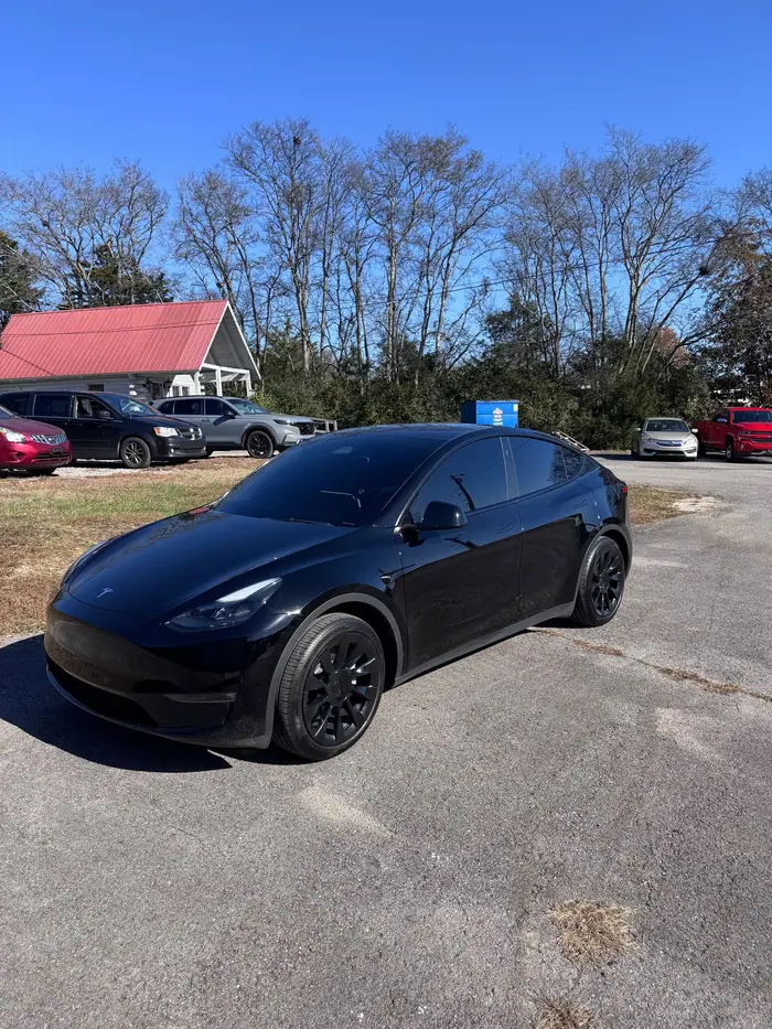 Blacked-out Tesla Model Y in the lot at the Stealth Tint and PPF shop on Highway 109, red-roofed buildings behind