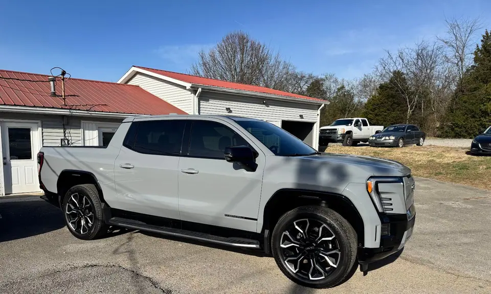 Gray GMC Sierra EV pickup with tinted windows in front of the red-roofed Stealth Tint and PPF shop